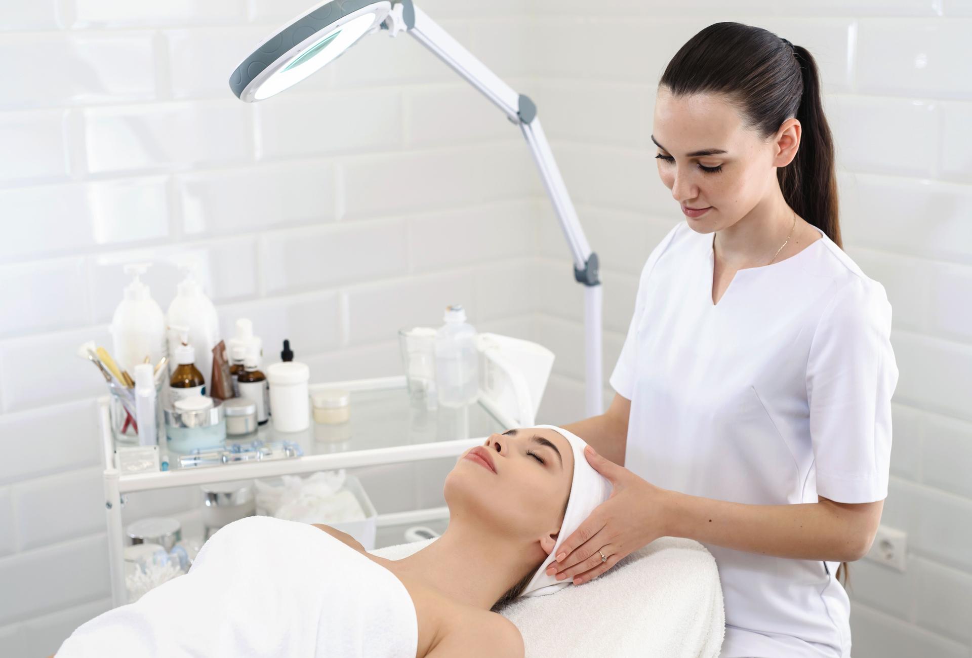 Cosmetologist at work. Young woman doctor preparing patient to beauty procedures. Puts a headband on customer's head to close a hair. Healthy lifestyle. Female beautician