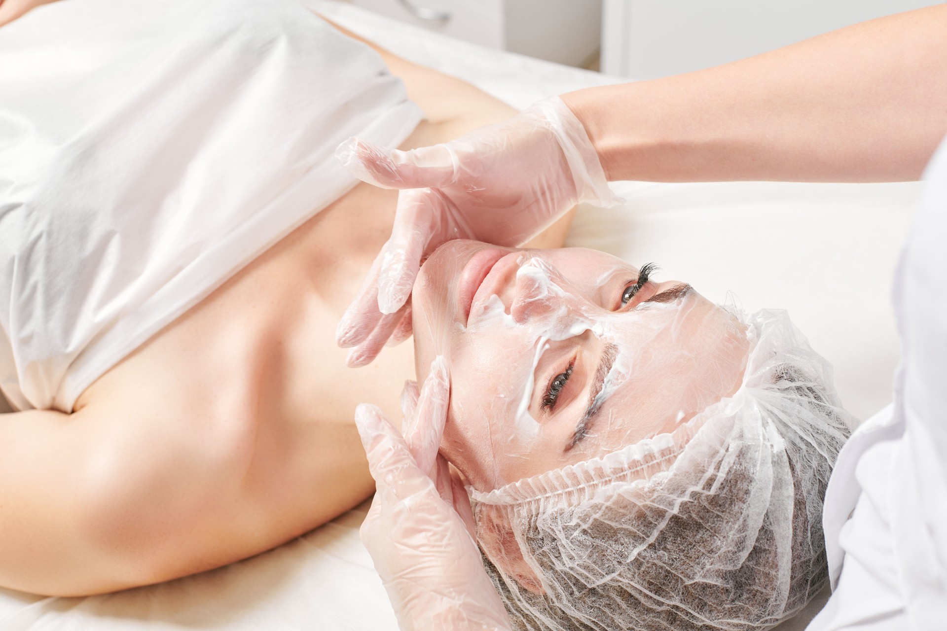 Cosmetologist massages cream mask into woman face skin for rejuvenation, procedure in beauty salon