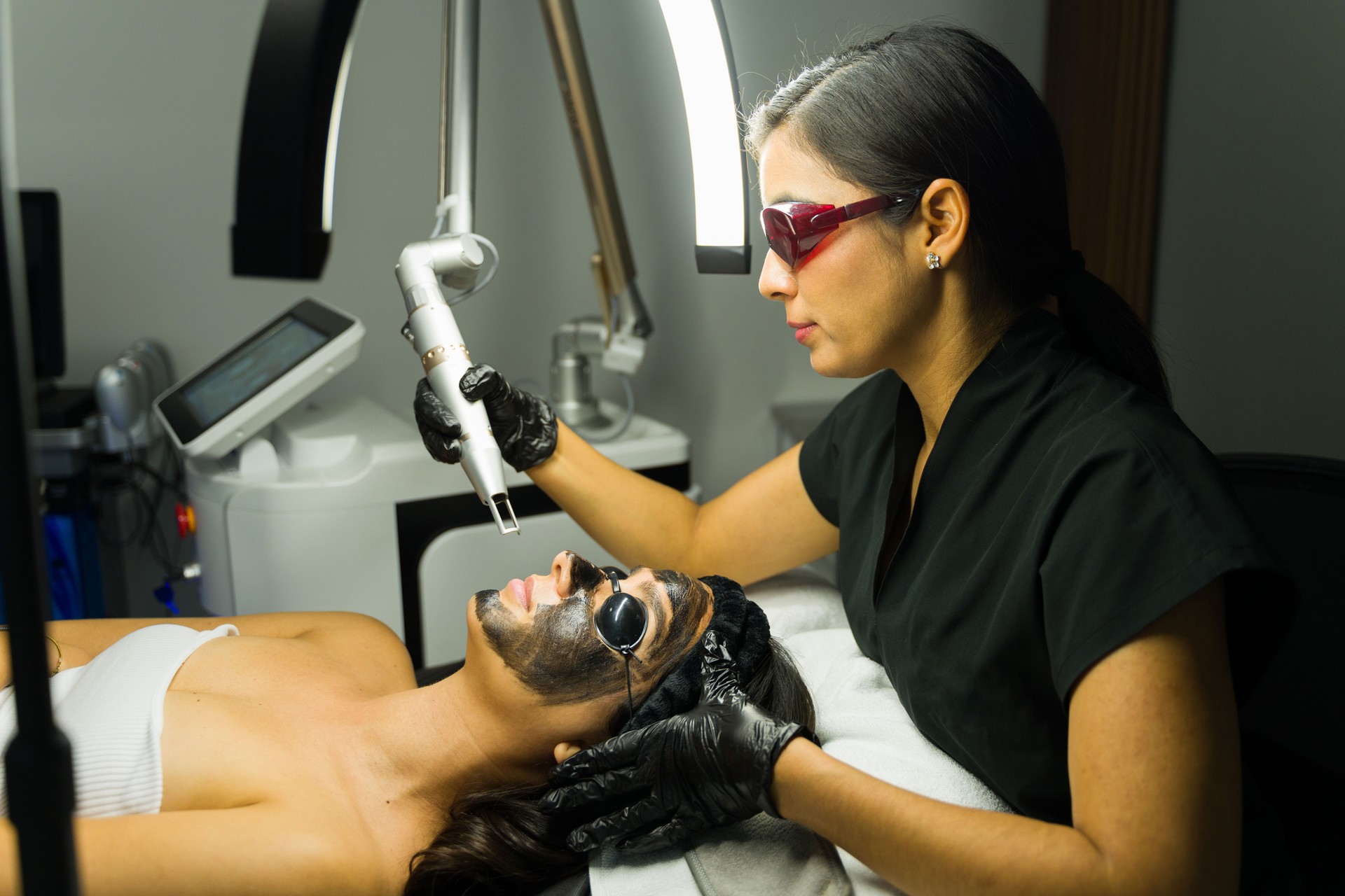 Woman undergoing a YAG laser treatment with a carbon mask by a skilled beautician in a modern medical beauty clinic setting