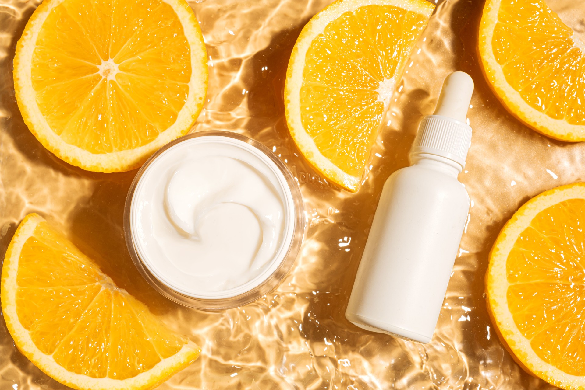 Cosmetic products in yellow water background with orange citrus