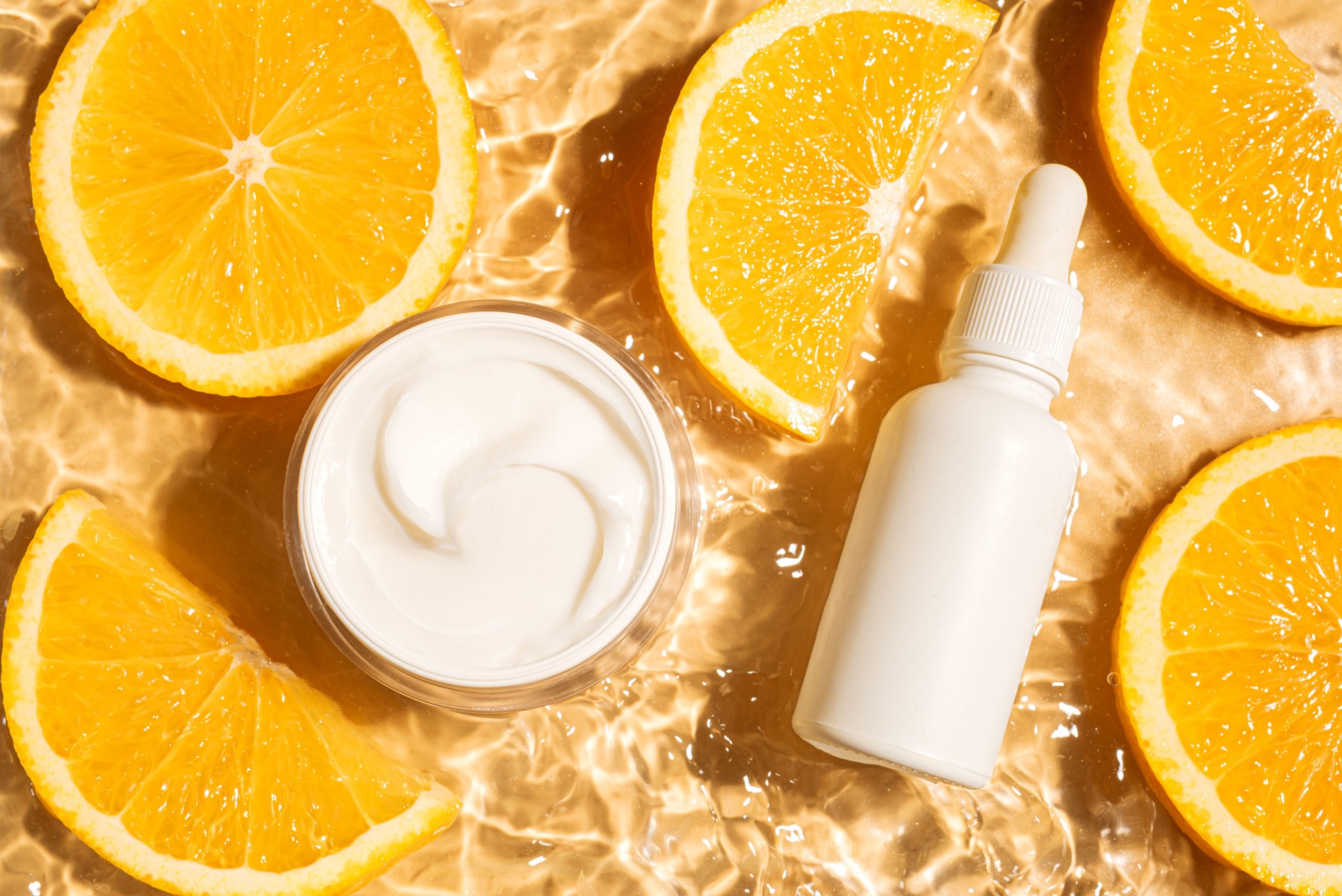 Cosmetic products in yellow water background with orange citrus