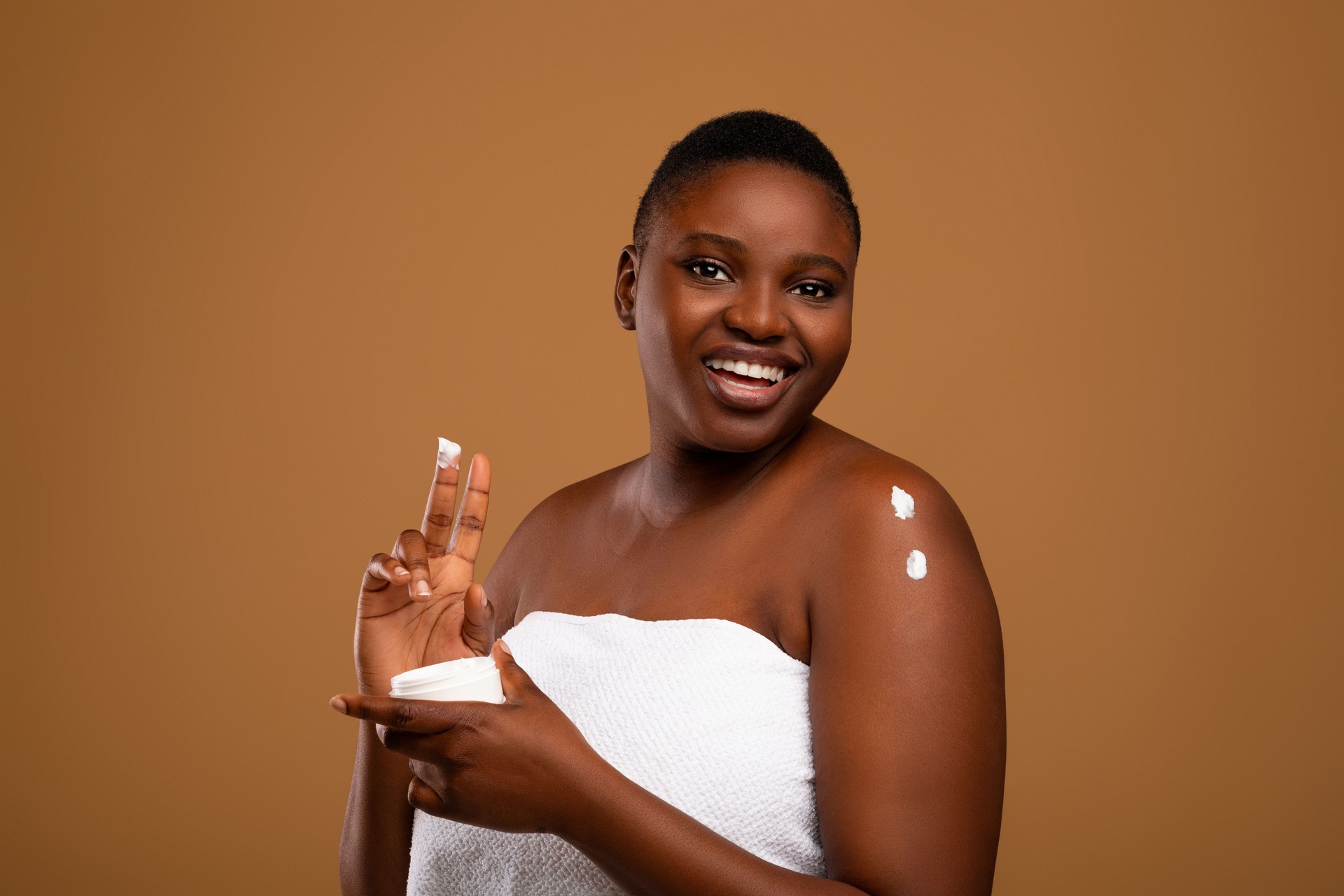 Beautiful young african american woman applying body moisturizer